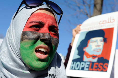 Una mujer con la cara pintada con los colores de la bandera Libia sujeta una foto de Gadafi