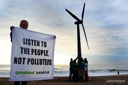 Activistas de Grennpeace ponen un molino eólico de madera y una chica sujeta una pancarta que dice: las persons no contaminan