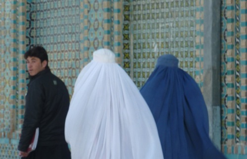 Dos mujeres con burka acompañadas de un joven que mira hacia la cámara con desconfianza