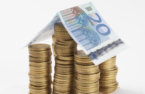Columnas de monedas de euro con un billete de 50 euros a modo de tejado 