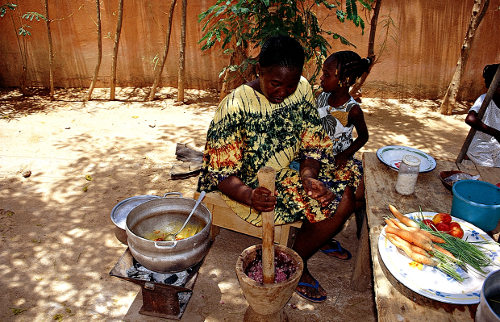 Una mujer con una niña en sus rodillas prepara, en el patio de su casa la comida