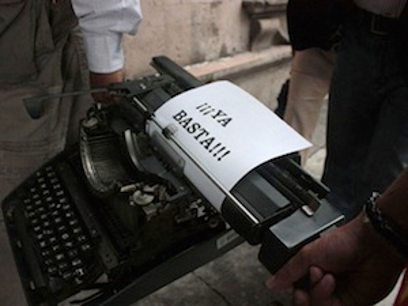 Dos hombres llevan una vieja máquina de escribir, el papel dice Ya basta
