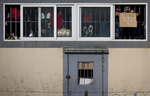 Inmigrantes tras las ventanas con rejas muestran pancartas 