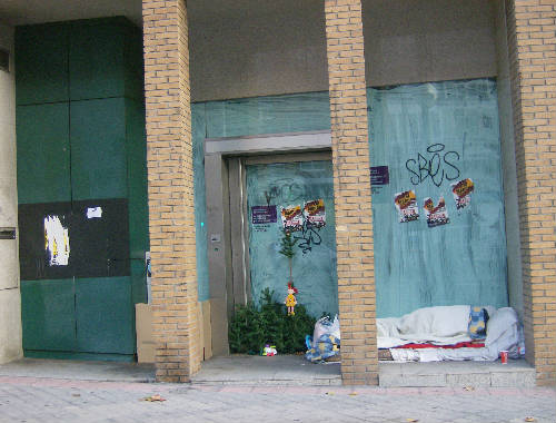 Hombre durmiendo en la calle en puerta banco cerrado