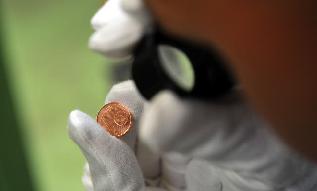 Un hombre con guantes blancos y una lupa examina una moneda de euro