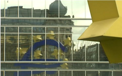 La escultura del euro se refleja en los cristales del edificio