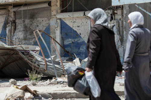 Mujeres pasean delante de una tienda destruida en Qusayr