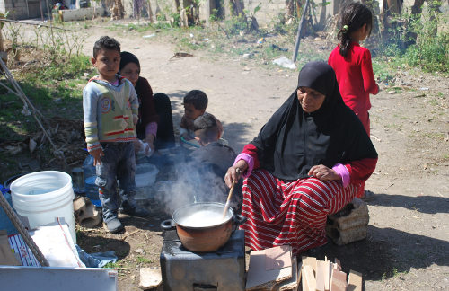 Varios niños y una mujer que prepara la comida en un fuego en el suelo en mitad del campo