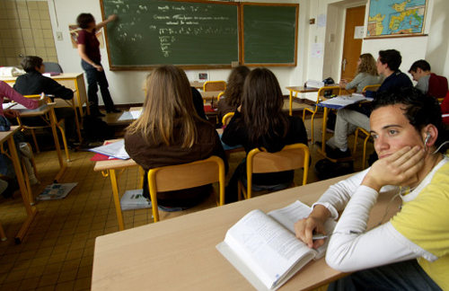 Un alumno escuchando música y mirando al vacío mientras los demás atienden a la profesora