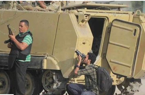 Un periodista toma una foto detrás de un carro de combate y un hombre armado