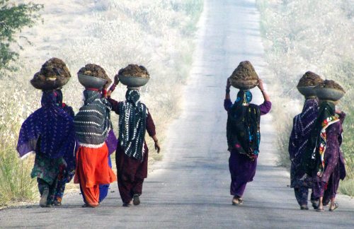 Mujeres de Pakistán caminan por una carretera con grandes pesos sobre la cabeza