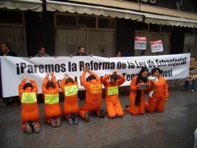 Activistas con mono naranja ante una pancarta que dice Paremos la reforma de la ley de extranjería