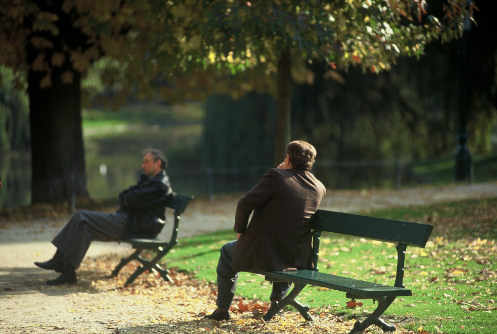 Dos hombres sentados en sendos bancos de un parque mirando a la nada