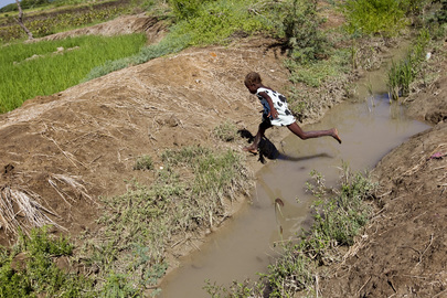 Una niña salta de un lado a otro de un canal de agua parda