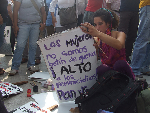 Una chica sentada en el suelo confecciona un cartel contra los feminicidios