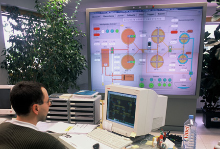 Un hombre delante de un ordenador y una pantalla con datos al fondo