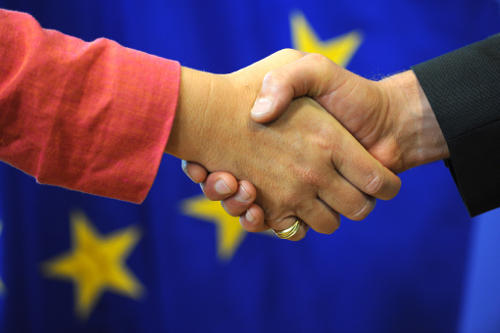 Simbólico apretón de manos ante una bandera de la UE