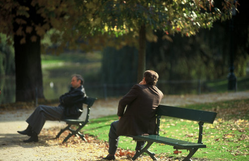 Dos hombres sentados en sendos bancos de un parque