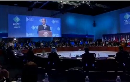 Mesa redonda de conversaciones y al fondouna pantalla en la que se ve al presidente de México hablando