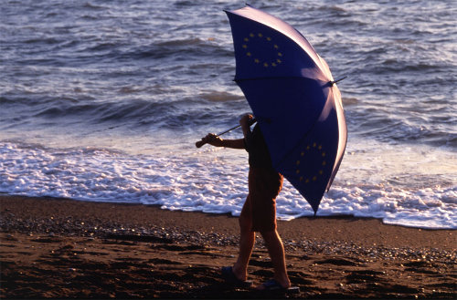 Un niño por la orilla de la playa se tapa con una sombrilla con la bandera de Europa