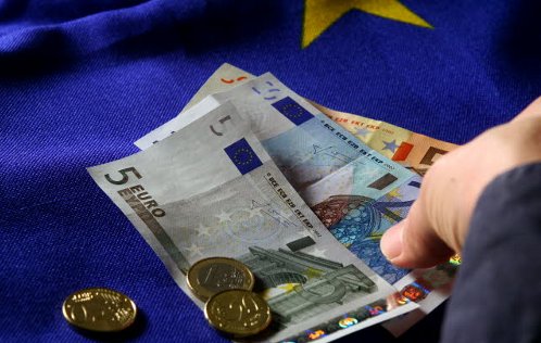 Sobre un fondo de la bandera de Europa una mano entrega billetes de euro