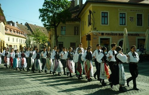 Una larga fila de jóvenes ataviados con los trajes típicos desfilan en la plaza de Sibiu