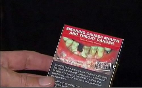 Un hombre muestra una cajetilla con la foto de una boca destruída por el tabaco