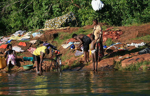 Mujeres, niños y un hombre lavan ropa y una bicicleta en el río