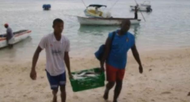 Dos pescadores de Mauricio llevan una caja de pescado junto a la playa