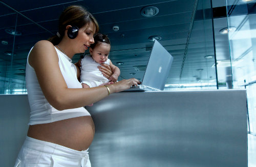 Una mujer embarazada con un bebé en brazos trabaja con un ordenador