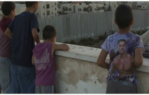 Niños palestinos mirando desde un tejado el muro que rodea su casa