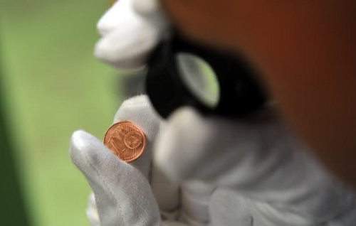 Una operario con guantes blancos examina con una lupa una moneda de 1 céntimo 