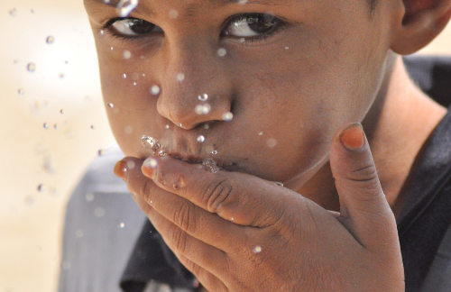 Un niño se lleva agua a la boca con la mano