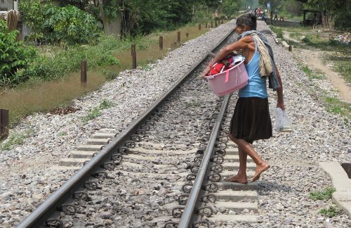 Una mujer cruza la vía con una palangana con ropa