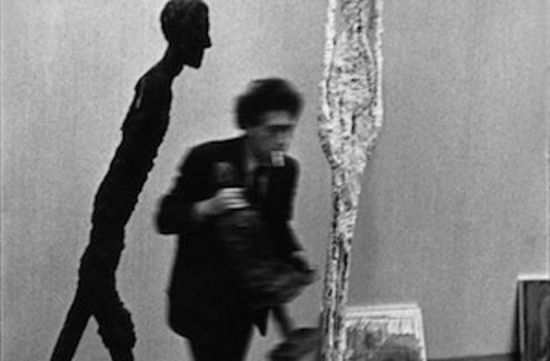 Giacometti con una escultura en la mano pasa al lado de otra escultura