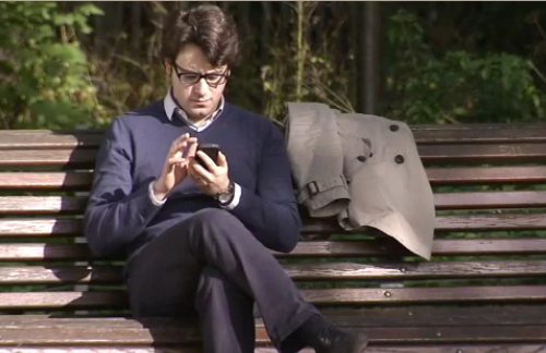 Un joven envía un SMS sentado en el banco de un parque