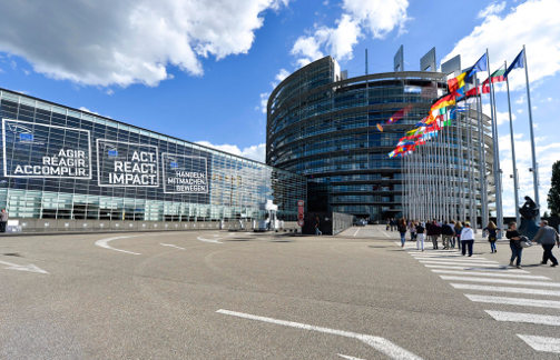 Edificio del Parlamento Europeo en una pantalla al lado una pantalla con el logo en varios idiomas 