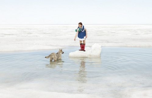 Una joven en medio de una extensión de agua sobre un montículo de hielo llama a su perro