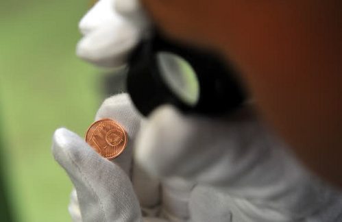 Un hombre mira una moneda de euro con una lupa