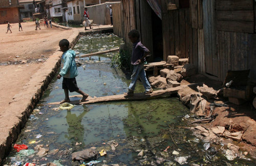 niños cruzan por encima de un canal por donde van las aguas sanitarias