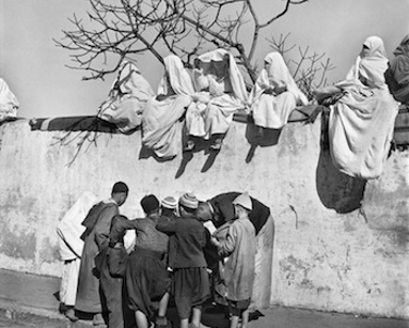 Mujeres marroquíes sentadas en una tapia y unos hombres abajo