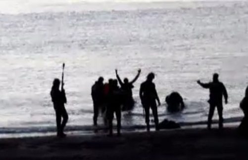 Guardias Civiles con armas disuasorias reciben a inmigrantes que llegan del mar con los brazos en alto