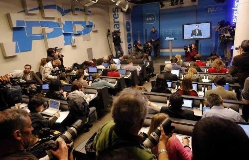 Sala de prensa con una pantalla al fondo desde la que habla Rajoy