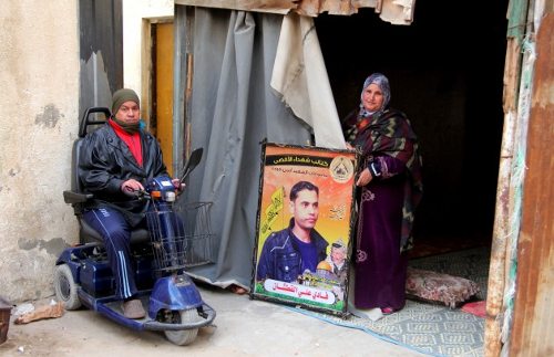 El padre de Fadi al Qutshan en silla de ruedas y su madre que muestra una foto de su hijo en la puerta de su casa