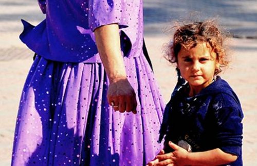 Una niña, junto a la falda de su madre, mira a la cámara