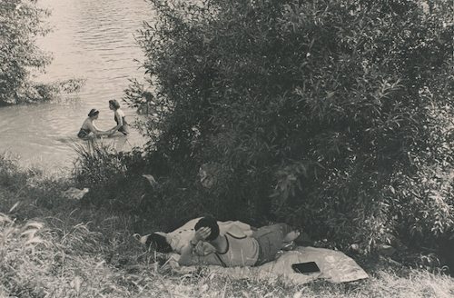Una pareja en la hierba mira a dos chicas que se bañan en el río