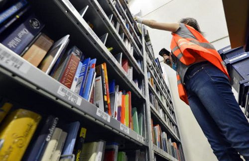 Una joven subida en una escalera chequea los libros de una estantería