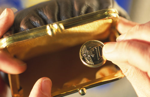 Una persona observa una moneda de euro que extrae de un monedero vacío