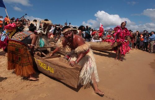 Guerreros climáticos vestidos con trajes de la región rodean sus canoas sobre la arena