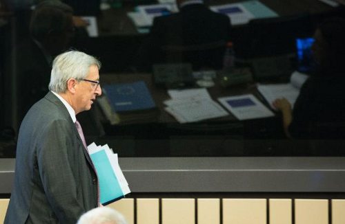 El presidente Juncker pasa delante de un cristal detrás del cual hay personas trabajando